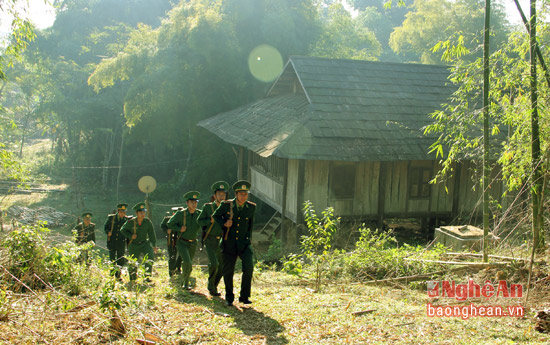Những người lính biên phòng hành quân đi tuần bên ngôi nhà đồng bào Thái lợp bằng mái sa mu.